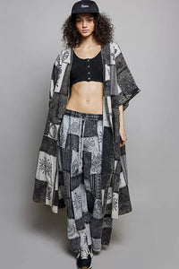 Woman wearing a long black and white patterned kimono over a black top and pants on a gray background