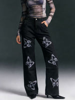 Black pants with butterfly patterns worn by a person on a gray background