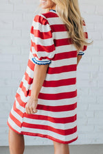 Woman wearing a red and white striped dress against a white brick wall.