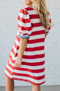 Woman wearing a red and white striped dress against a white brick wall.