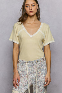 Woman wearing a light yellow top with lace trim and floral pants against a gray background