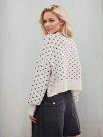 Woman wearing a white cardigan with black heart patterns against a light gray background