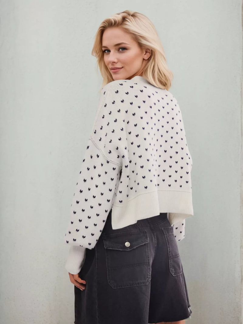 Woman wearing a white cardigan with black heart patterns against a light gray background