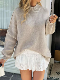 Woman wearing a beige sweater over a white lace dress, standing indoors.