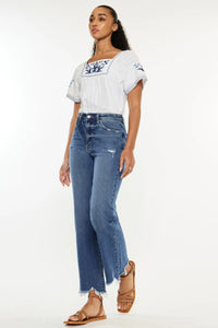 Woman wearing a white embroidered top and blue jeans on a white background
