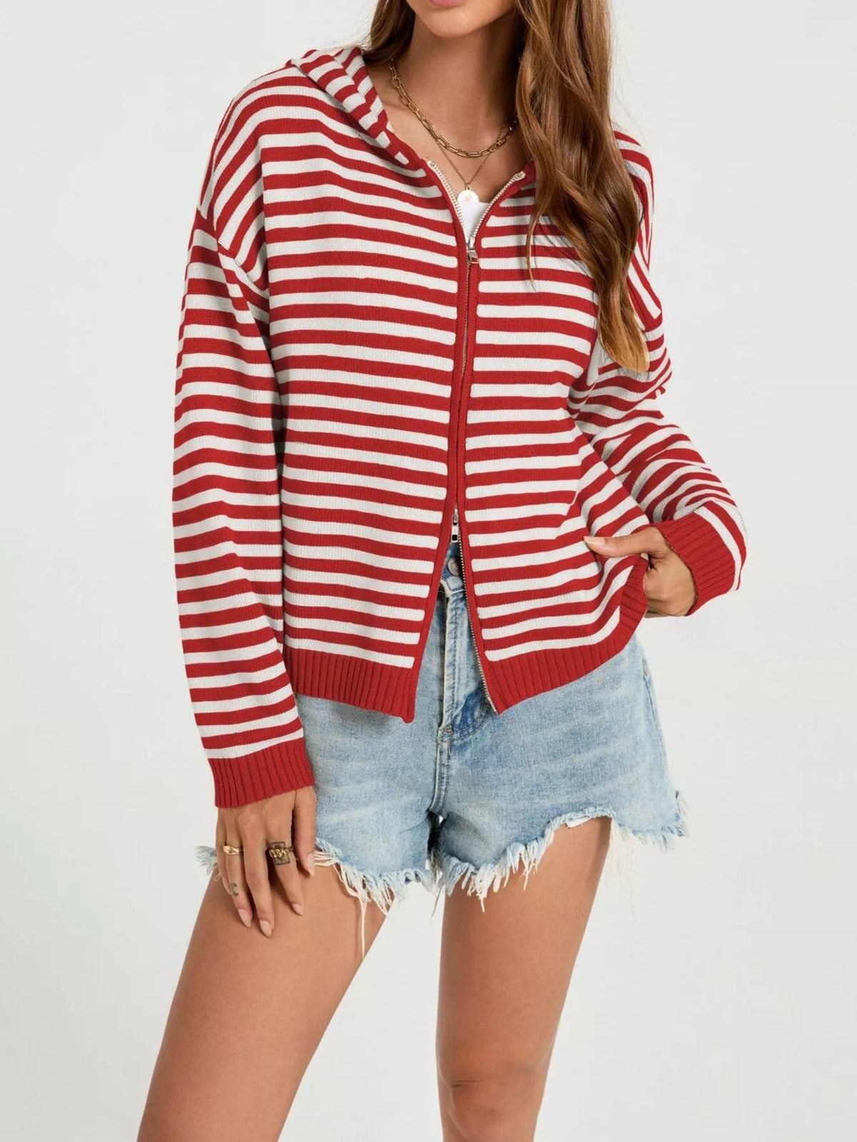 A woman wearing a red and white striped zip-up hoodie with a hood, paired with light-wash denim shorts, against a plain white background.