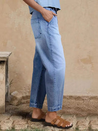 Person wearing light blue jeans standing against a beige wall.