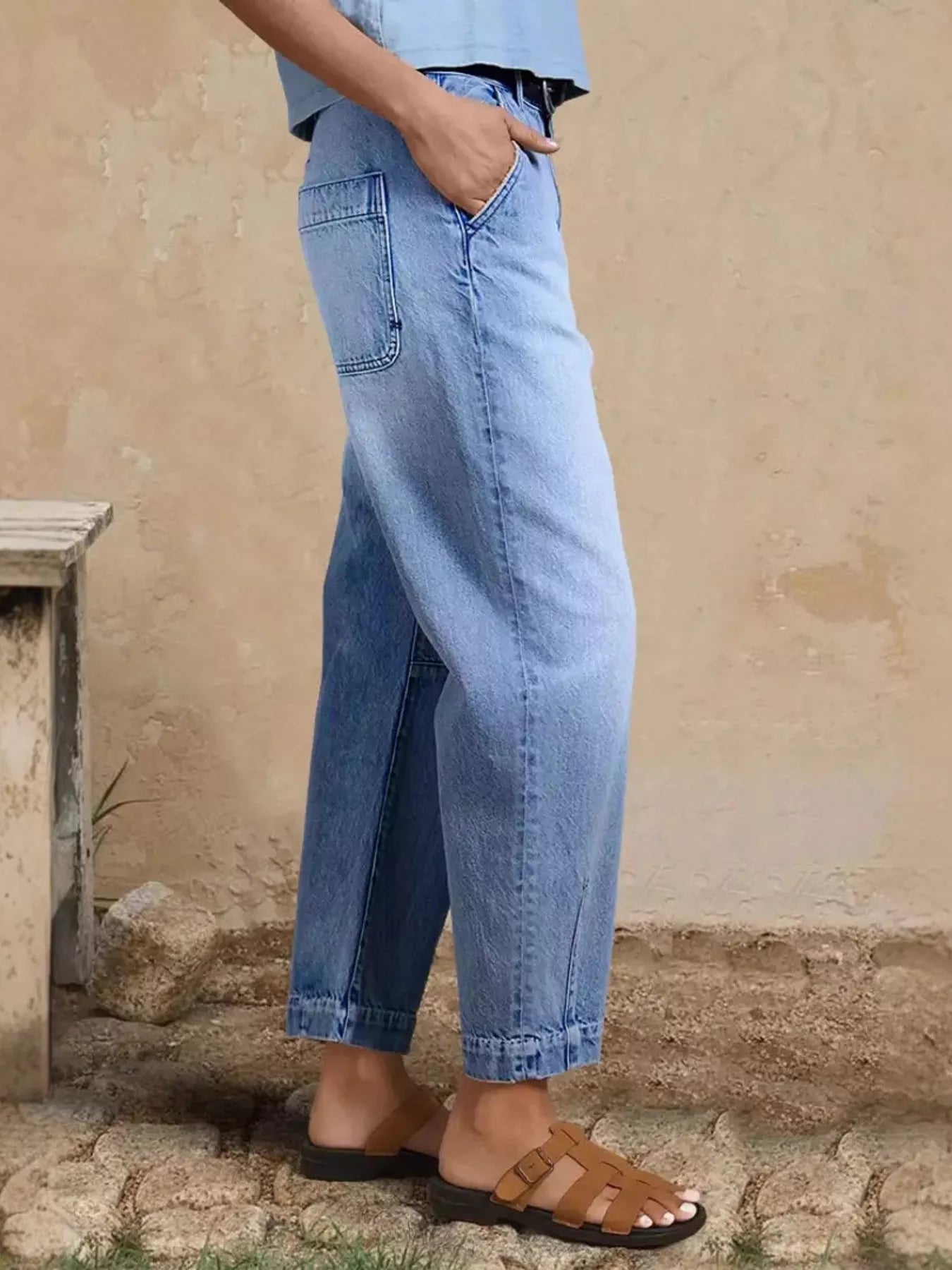 Person wearing light blue jeans standing against a beige wall.