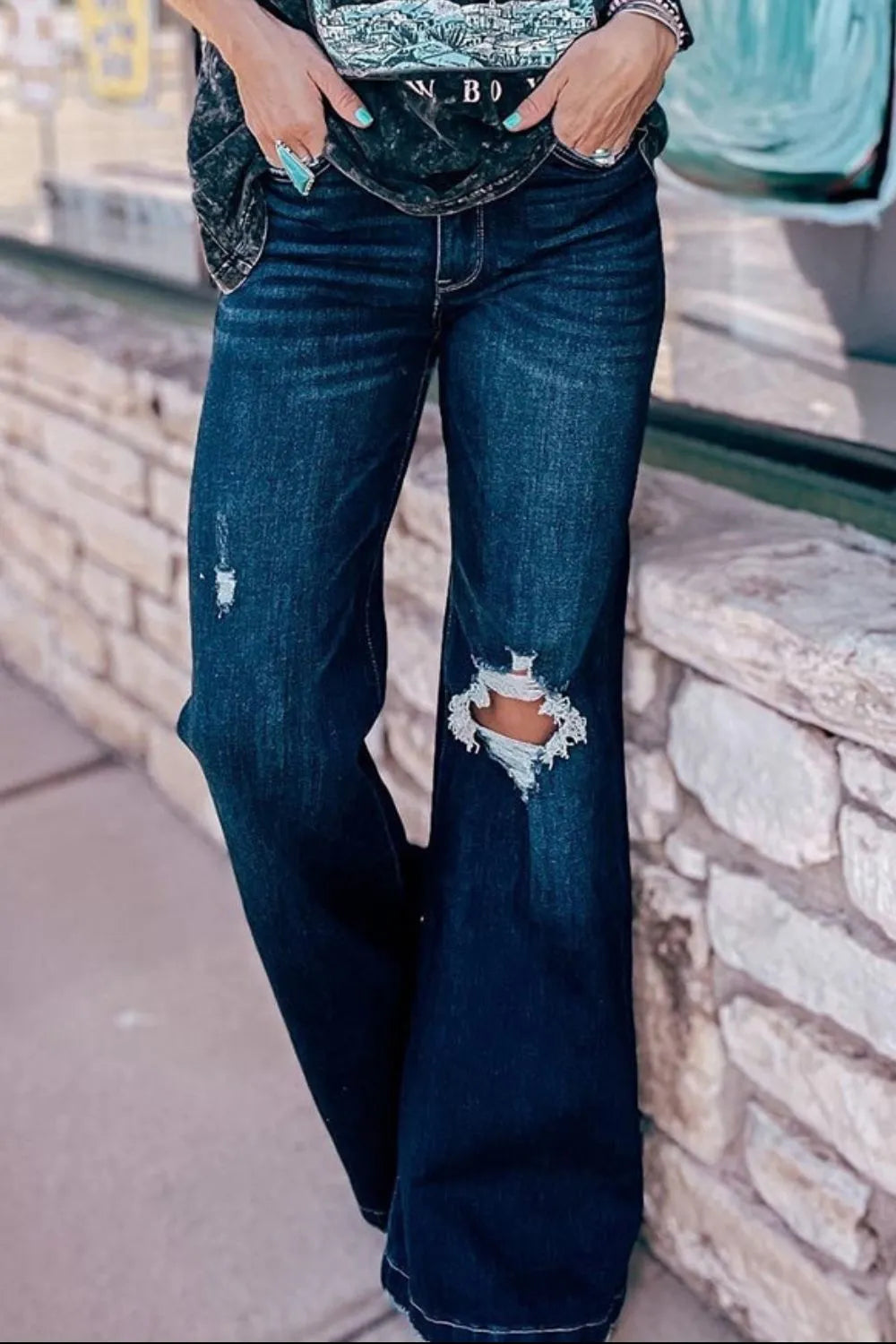 Person wearing distressed blue jeans standing against a stone wall.