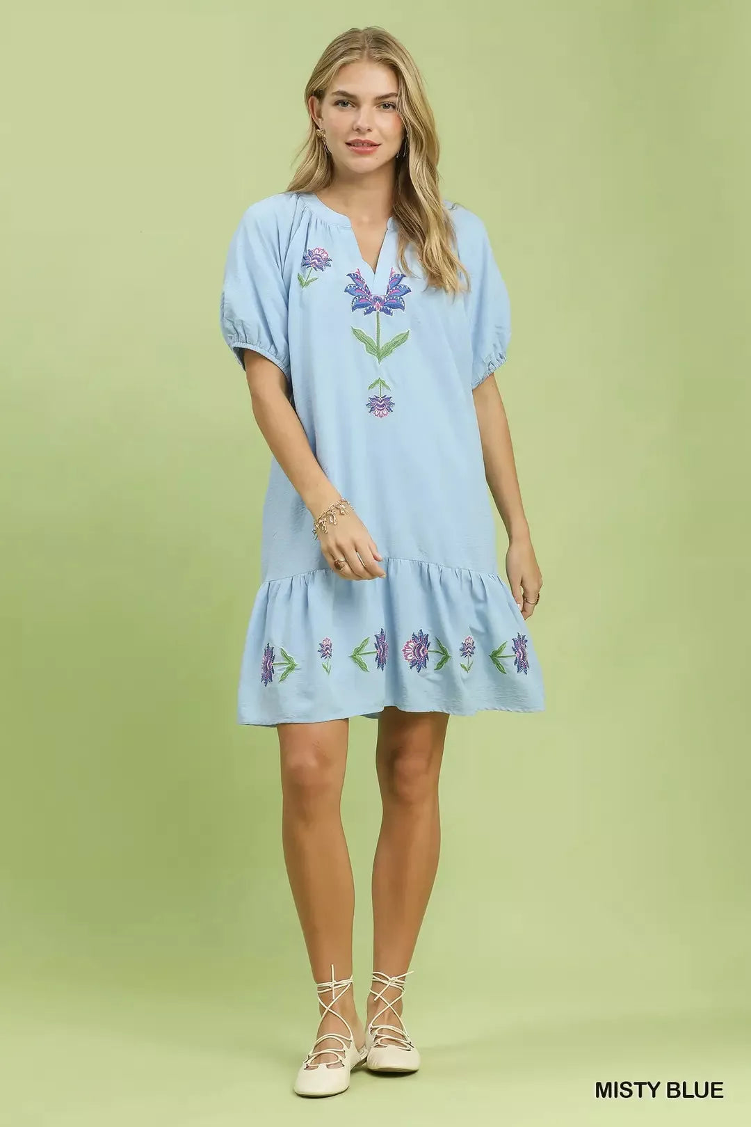 Woman wearing a light blue dress with floral embroidery on a green background