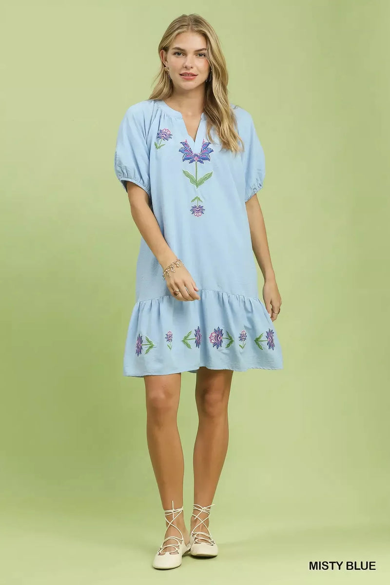 Woman wearing a light blue dress with floral embroidery on a green background
