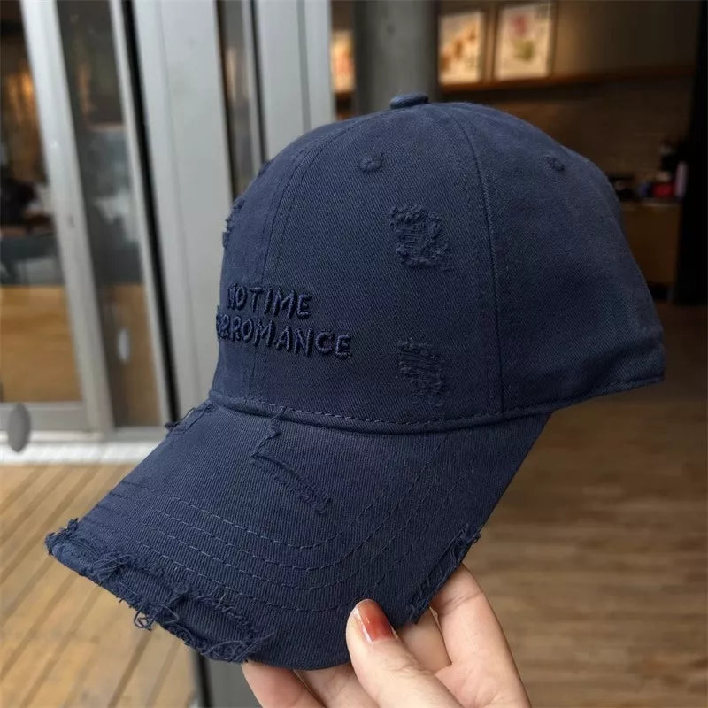 Navy blue distressed baseball cap with text held by a hand indoors.