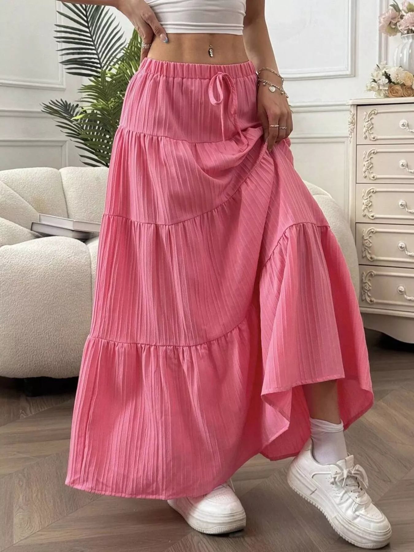 Person wearing a pink tiered skirt with white sneakers in a room setting.