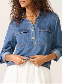 Woman wearing a blue denim jacket over a white dress on a plain background
