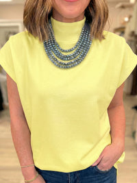 Person wearing a yellow top and blue jeans with a necklace in an indoor setting