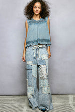 Woman wearing a denim outfit with a sleeveless top and patchwork pants against a gray background