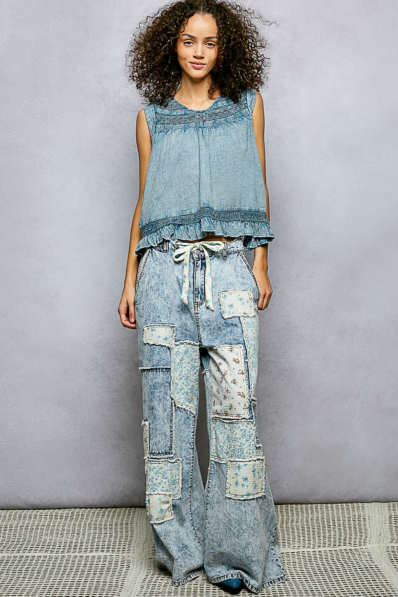 Woman wearing a denim outfit with a sleeveless top and patchwork pants against a gray background