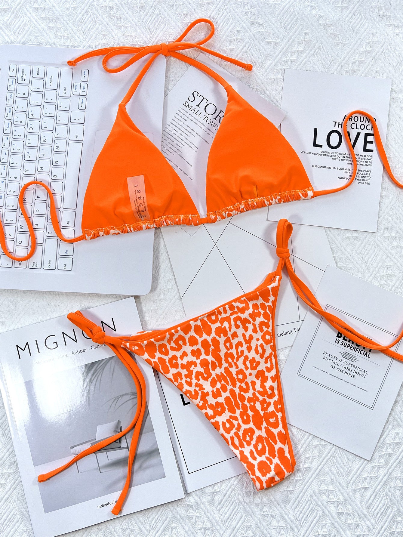 Orange bikini set with leopard print on a surface with magazines and a keyboard.