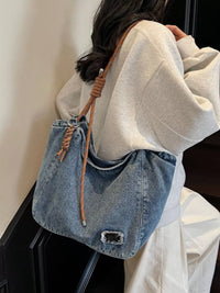 Person wearing a denim handbag with a brown strap against a neutral background