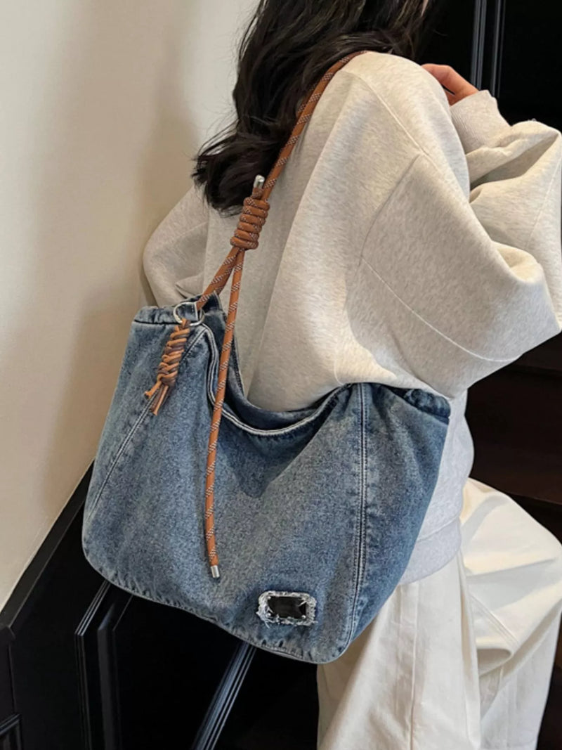 Person wearing a denim handbag with a brown strap against a neutral background