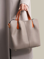 Person holding a gray handbag with brown handles against a neutral background