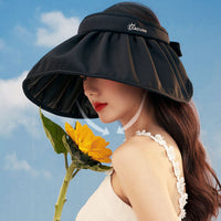 Woman wearing a black visor with a yellow flower against a blue sky.