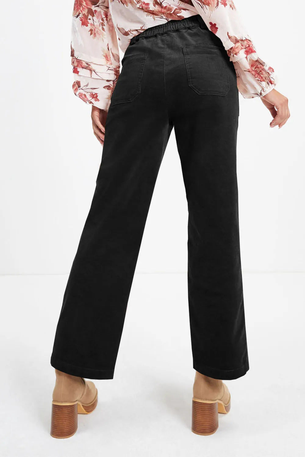 Black wide-leg pants worn with a floral blouse on a white background