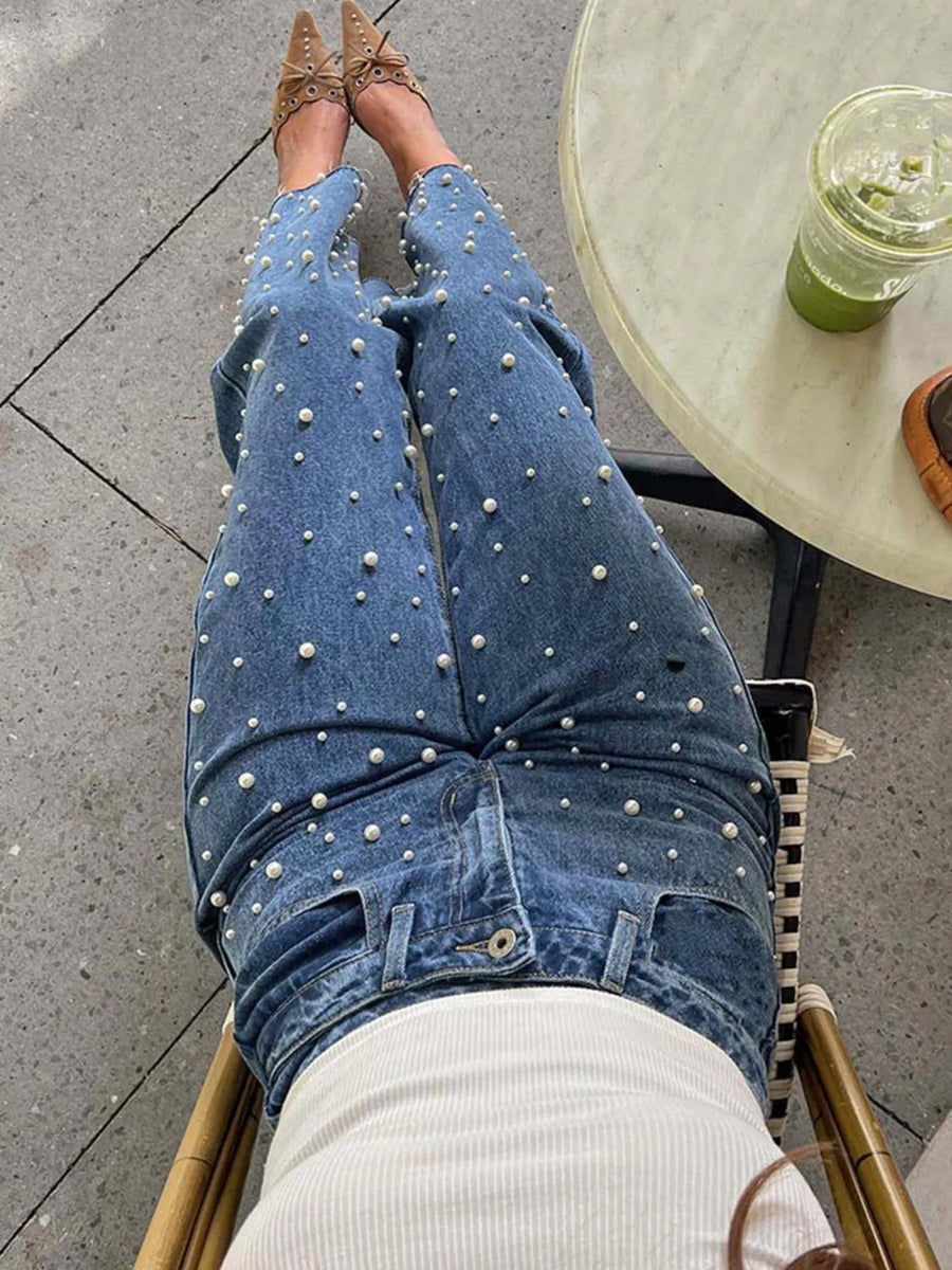 Person wearing blue jeans with white embellishments sitting on a chair outdoors.