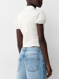 Person wearing a white blouse with puffed sleeves and light blue jeans on a plain background