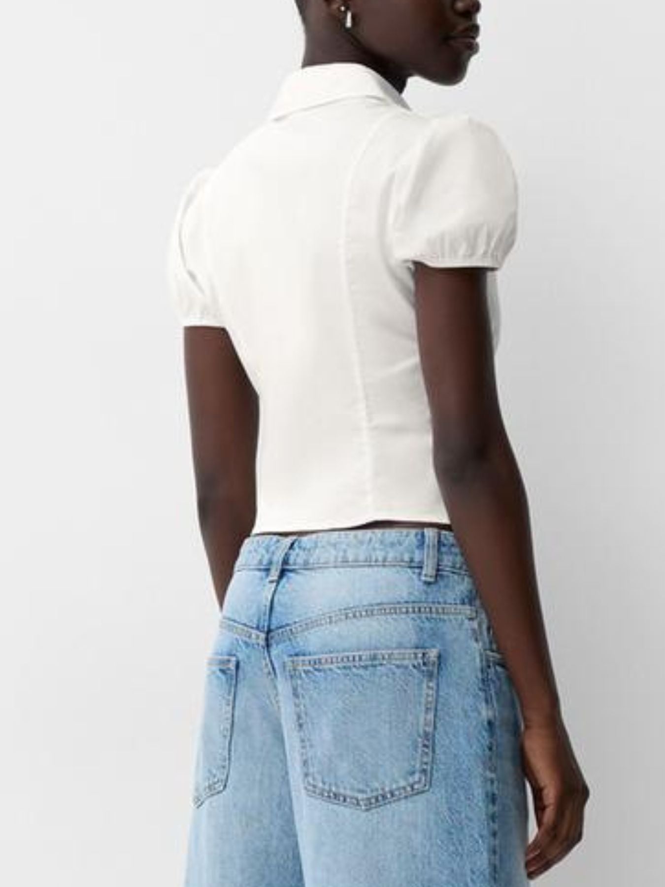 Person wearing a white blouse with puffed sleeves and light blue jeans on a plain background