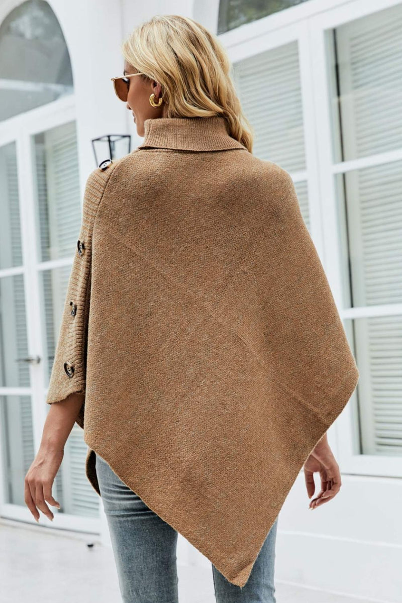 Woman wearing a brown poncho in front of a white building.