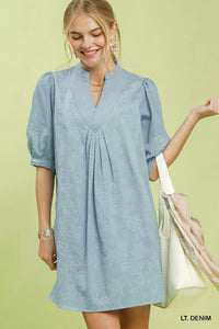 Woman wearing a light denim dress against a green background