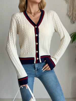 Person wearing a white cardigan with blue and red accents and blue jeans.