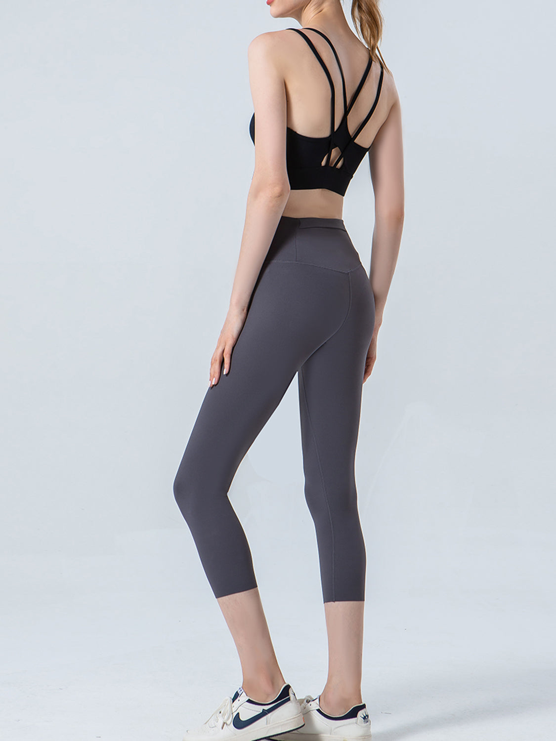 Person wearing a black sports bra and gray leggings on a white background
