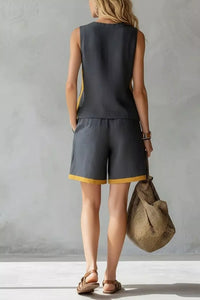 Person wearing a dark sleeveless top and shorts with yellow trim, holding a woven bag against a plain background.