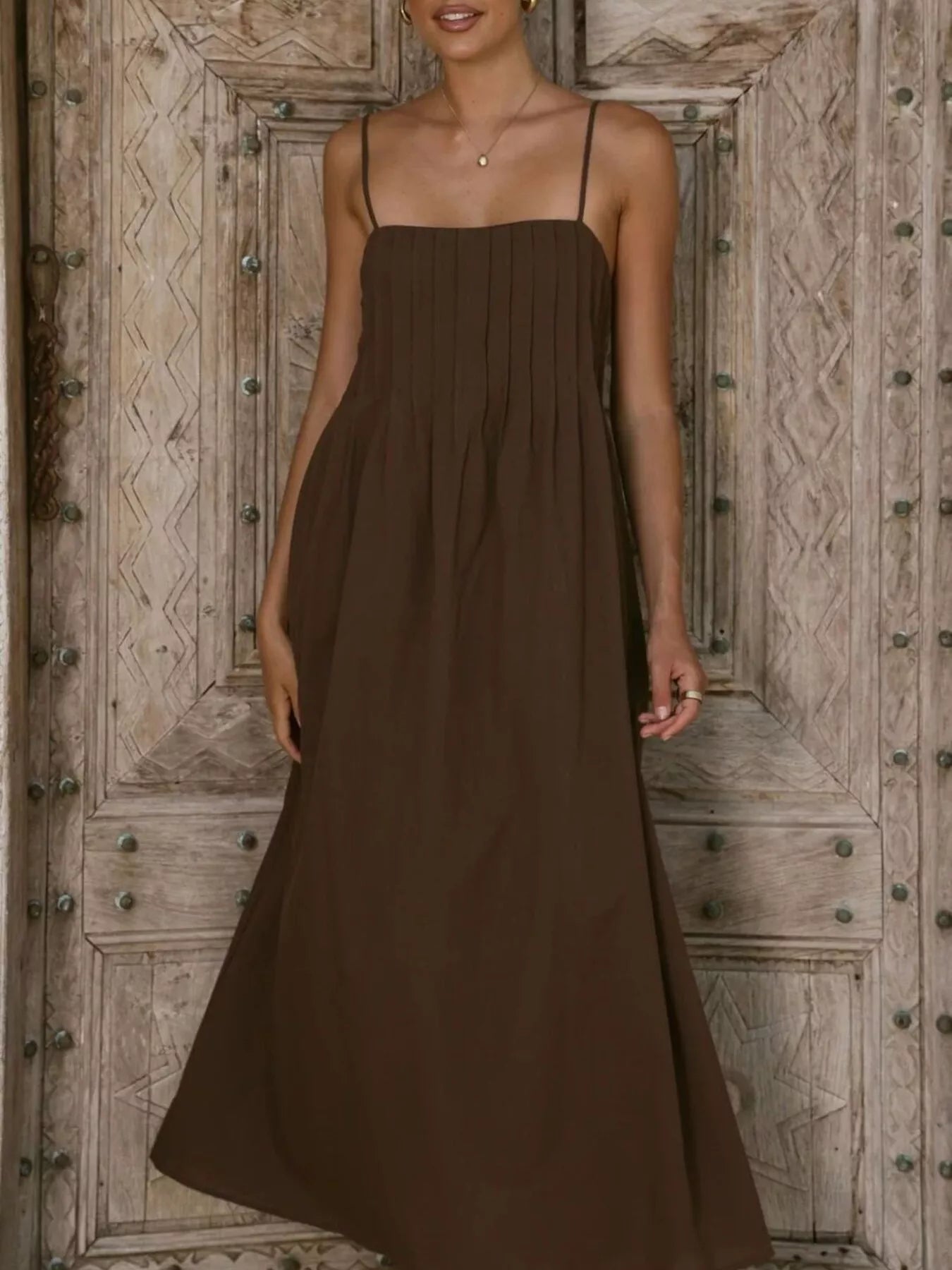 Woman wearing a brown dress standing in front of a wooden door.