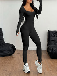 Person wearing a black jumpsuit with white sneakers in a minimalistic room.