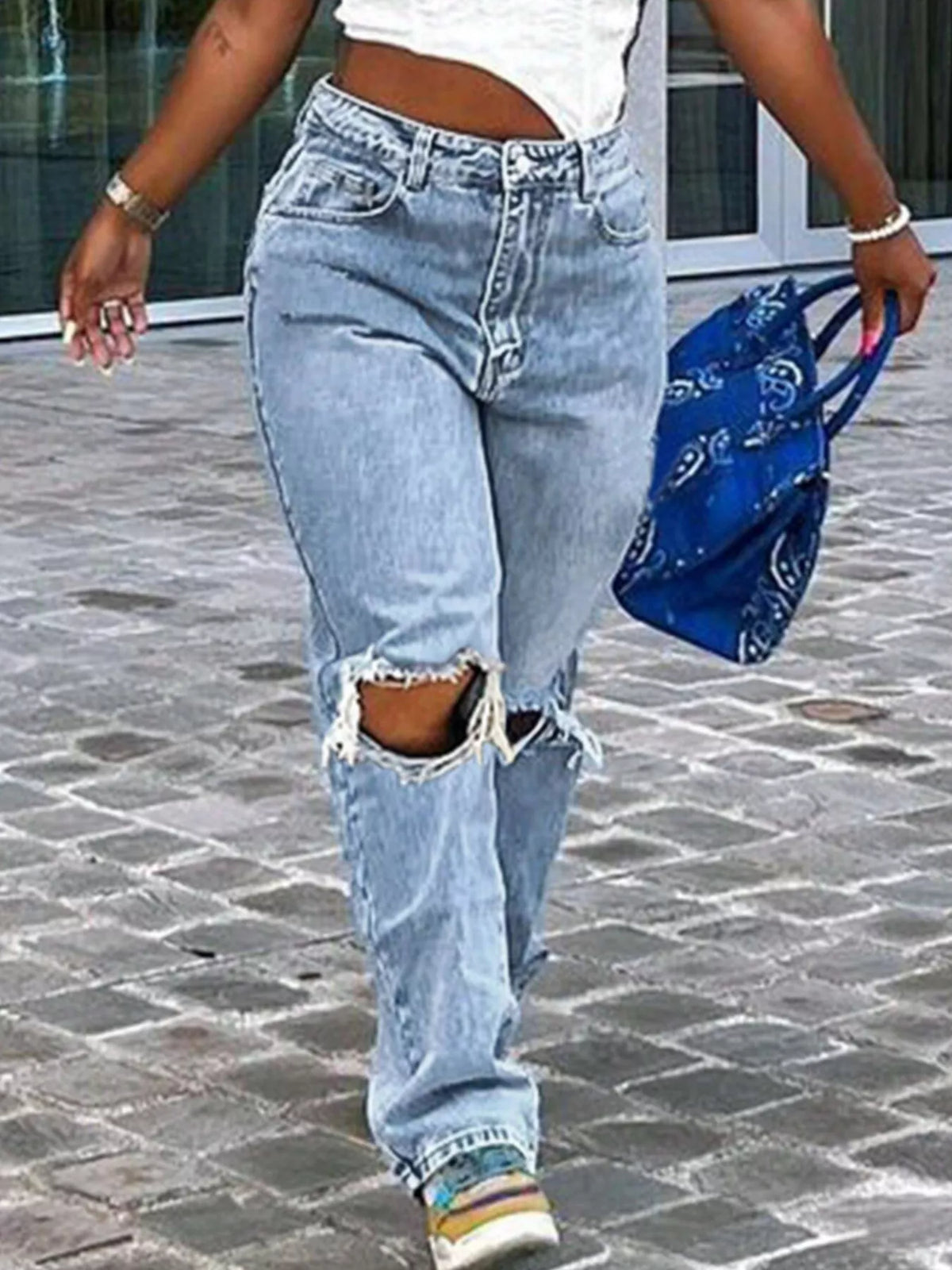 Person wearing ripped light blue jeans walking on a stone pavement.