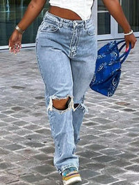Person wearing ripped light blue jeans walking on a stone pavement.