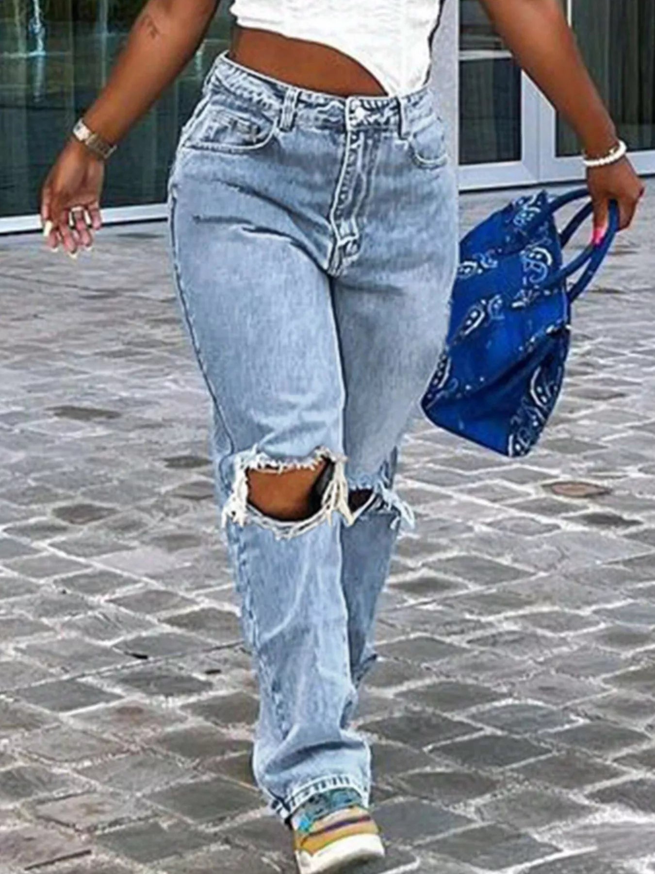 Person wearing ripped light blue jeans walking on a stone pavement.