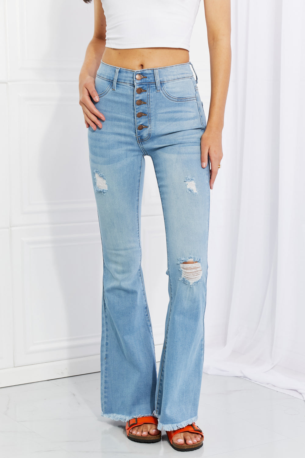 A pair of blue flare jeans with a high waist, button down front, and distressed details such as a frayed hem and pockets.