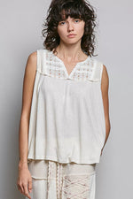 Woman wearing a white sleeveless top with lace details against a gray background