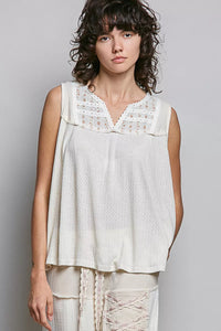 Woman wearing a white sleeveless top with lace details against a gray background