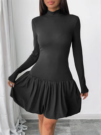 Black long-sleeve dress with a ruffled skirt worn by a person against a white curtain background.