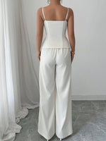 Person wearing a white top and pants standing in front of a white curtain.