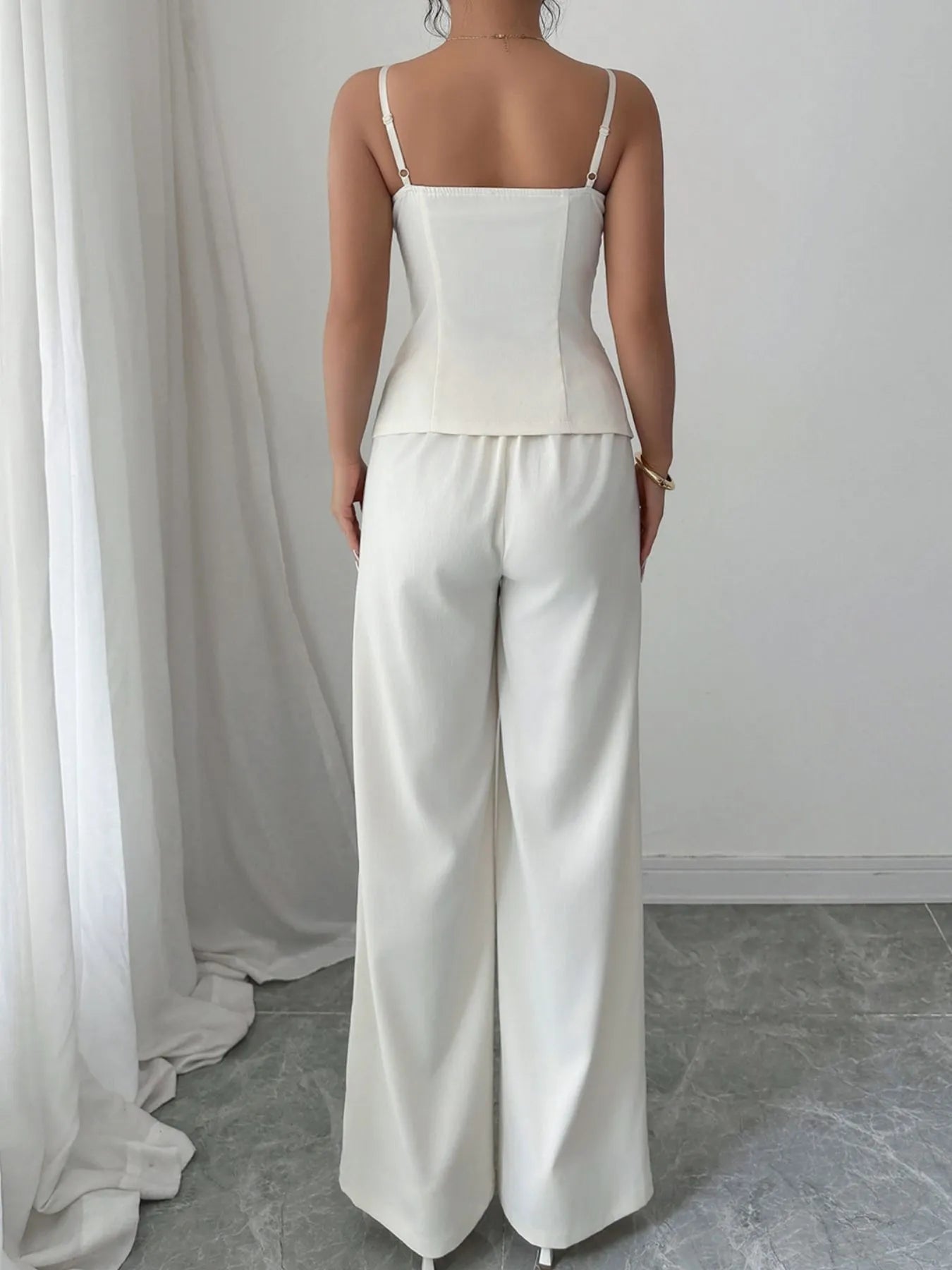 Person wearing a white top and pants standing in front of a white curtain.