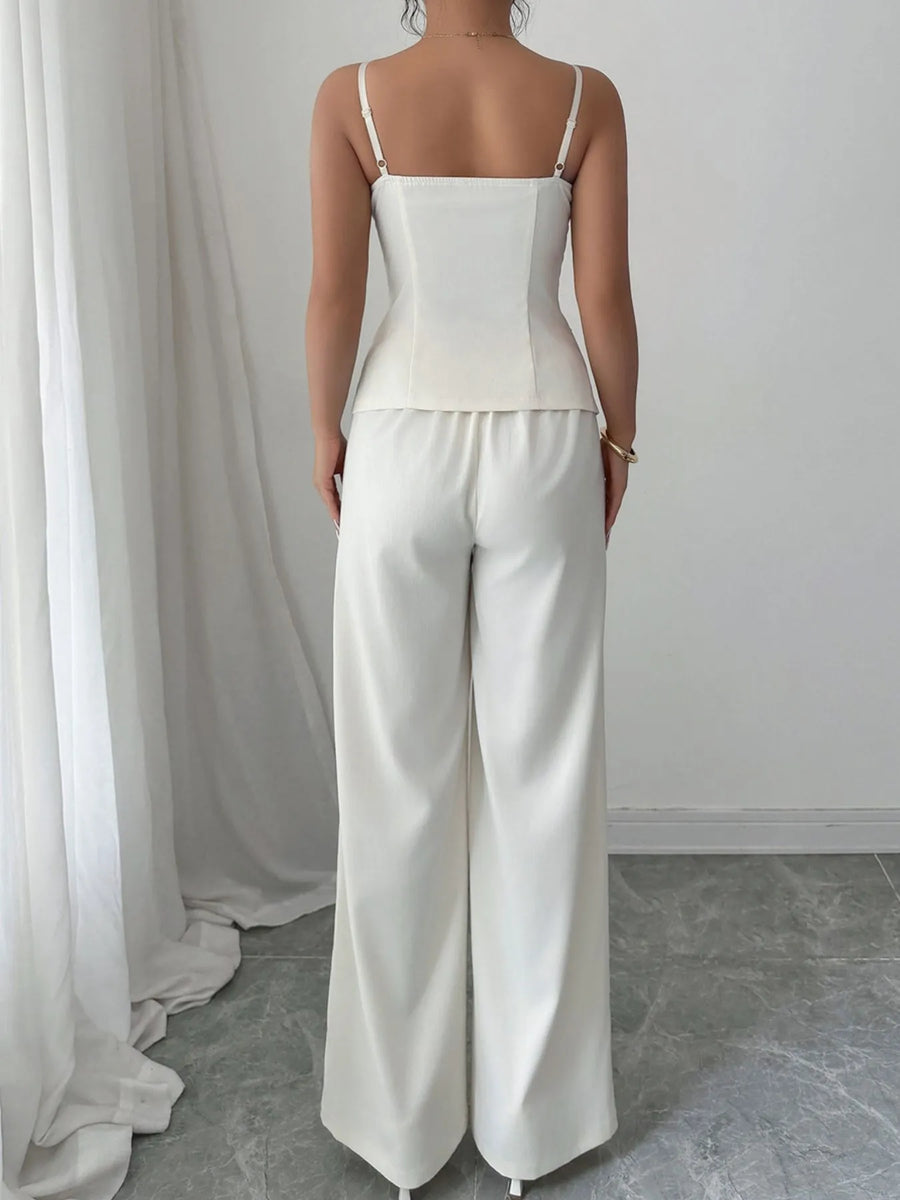 Person wearing a white top and pants standing in front of a white curtain.