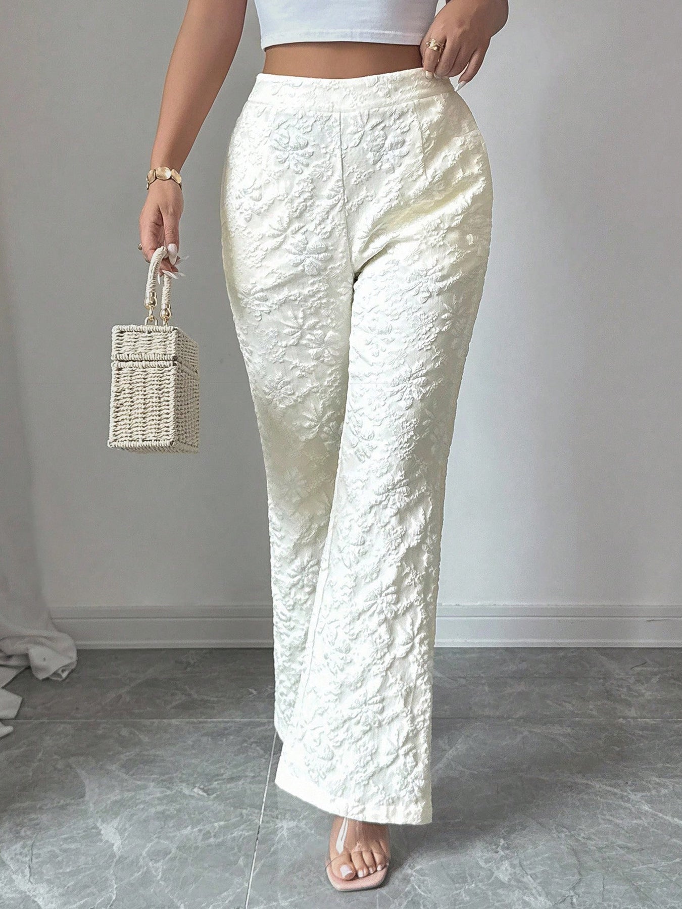 Person wearing textured white pants holding a woven bag against a plain background