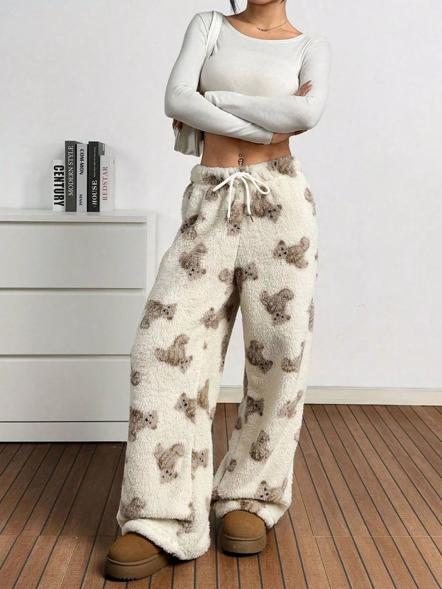Person wearing patterned pajama pants and a light gray long-sleeve top in a minimalistic room.
