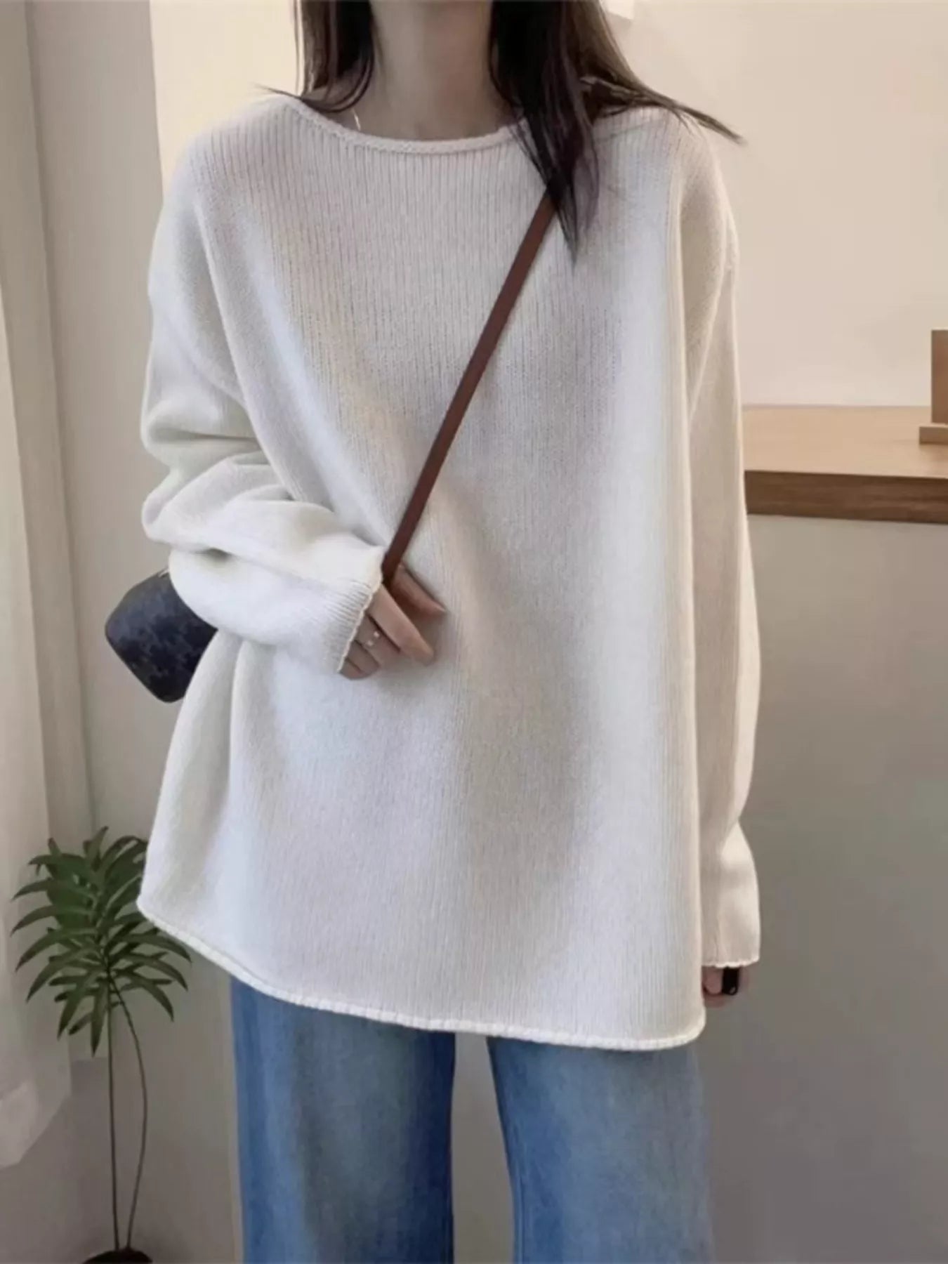Person wearing a white sweater and blue jeans in an indoor setting